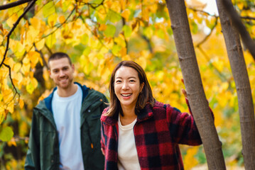 Happy interracial couple walking and holding hands in autumn forest.