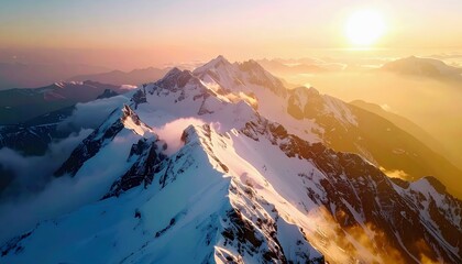 Aerial view of dramatic, snow-covered mountain ranges at sunset, with clouds creating a mystical atmosphere.