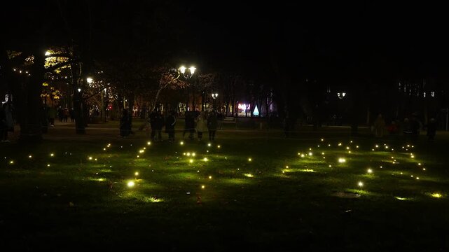 Night park in Riga, Latvia shows warm yellow ground lights, a triangular tree sculpture, streetlamps, and visitors moving slowly during Staro Riga 2025