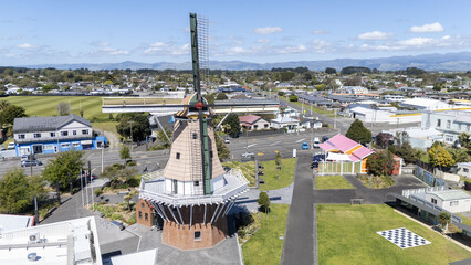 Aerial view of De Molen windmill, a towering structure with intricate brickwork and sails against a backdrop of green fields, Foxton, Manawatu-Whanganui Region, New Zealand.