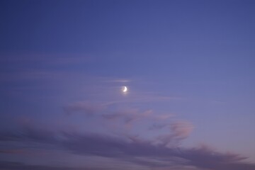 Crescent moon shines brightly in the evening sky with soft clouds and a purple hue sky 90