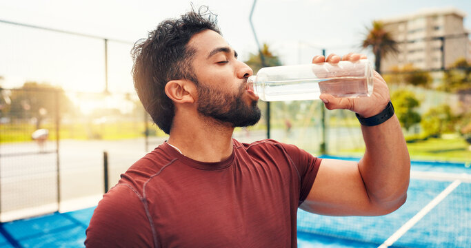 Man, drinking water and break at tennis court, sports and hydration for wellness with exercise routine. Person, athlete and bottle for electrolytes, training or fitness with rest for game in city - Powered by Adobe