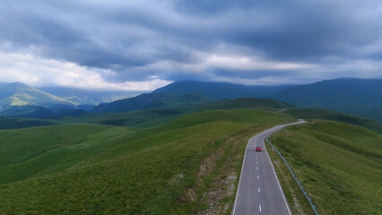 A red car is driving down a road in the Caucasus Mountains to the Dzhila-Su Valley