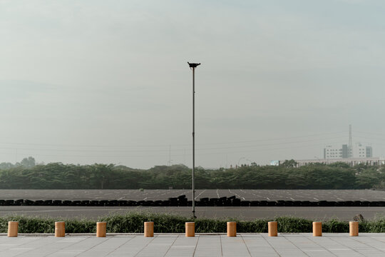 Tall street lamp pole in empty paved parking lot with tire barriers and blue sky in urban landscape.