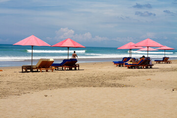 Beach Scene with Pink Umbrellas and Lounge Chairs on Sandy Shore with People Relaxing and Ocean Waves