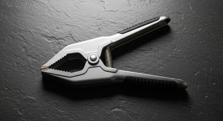 Silver spring clamp with textured grips resting on a dark stone surface in soft light.