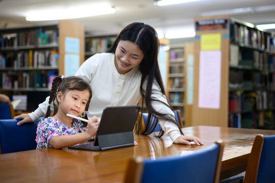 Asian woman teaching little girl to use digital tablet in library, learning together