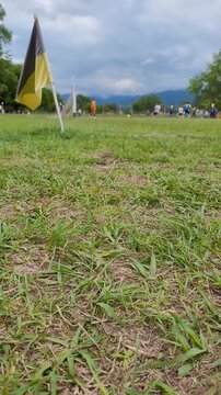 People playing soccer in the distance on a natural, green field with a border flag waving in the wind