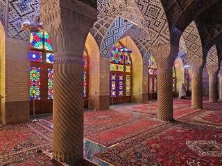 view of the vibrant stained glass windows reflecting hues of red and blue onto the ornate carpets of the Nasir-ol-Molk Mosque, Shiraz, Iran.