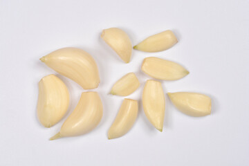 A small cluster of peeled, light-colored garlic cloves is scattered across a neutral white background, viewed from above