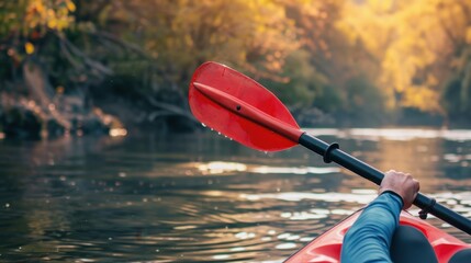 A person paddles a red kayak on a calm river surrounded by autumn foliage. The scene captures the tranquility of nature and outdoor activities.