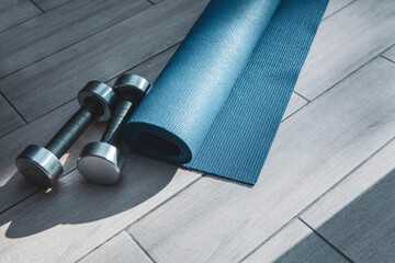 Exercise mat, towel, and metal dumbbells on a sunlit wooden floor create a calm home workout scene, symbolizing self-care, flexibility, strength training, and mindful fitness routines.