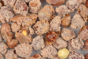 A close-up, full-frame view captures a pile of hazelnuts coated in a grainy, sugary crust, creating a dense, sweet texture