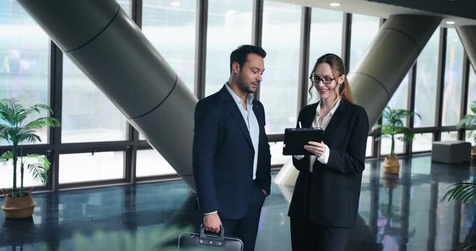 Businesswoman With A Tablet Discussing a Report With A Professional Businessman Holding a Brief Case In A Modern Office Atrium. - medium shot