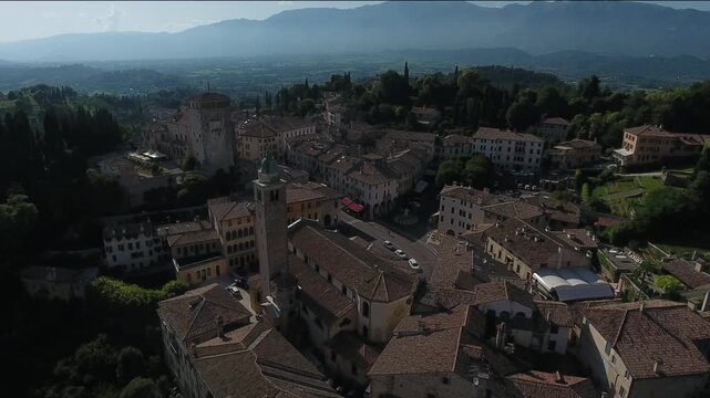 Aerial view of buildings with tiled roofs and mountains, the architecture contrasts with the natural landscape, creating a harmonious blend of textures, Asolo, Veneto, Italy.