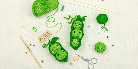 Handmade amigurumi peas with yarn, crochet tools, and work accessories on a fabric background