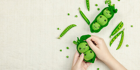 Hands holding crocheted pea toy among real pea pods on beige fabric. Natural colors