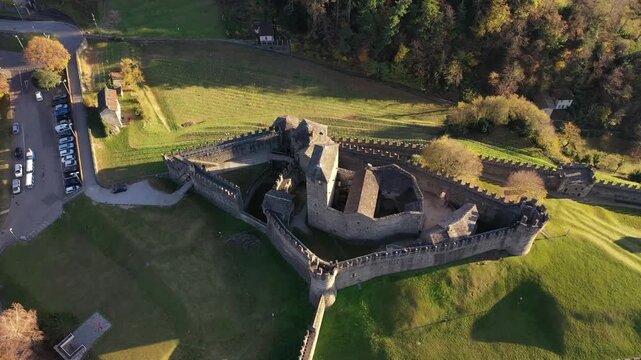 Aerial view of the Castel Grande fortress on a hill surrounded by green grass and trees, reflecting light and shadows, Bellinzona, Ticino, Switzerland.