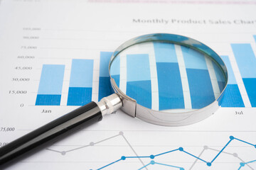 Magnifying glass on data business graphs paper.
