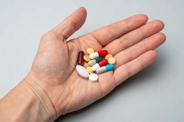 Closeup of a human hand displaying colorful medication pills and capsules on a neutral background, symbolizing healthcare, treatment, vitamins, supplements, pharmaceutical therapy, wellness, and 