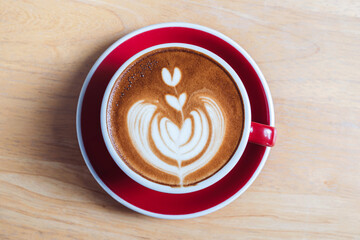 Top view of Hot coffee cappuccino latte art with small heart design in cup on red plate placed on wooden table in Cafe Shop in an atmosphere of relaxation.