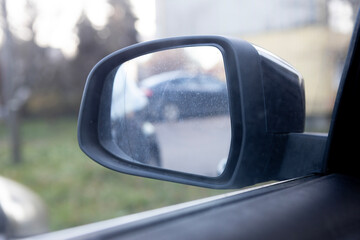 Car side mirror reflecting parking lot with cars and greenery in the background during daytime