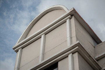 White concrete building facade featuring arched top design and vertical columns against blue sky.