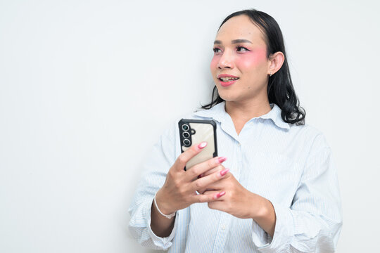 Portrait of a young Thai transgender person using phone against white background