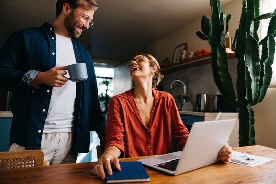 Happy couple laughing together with laptop and coffee at home - Powered by Adobe
