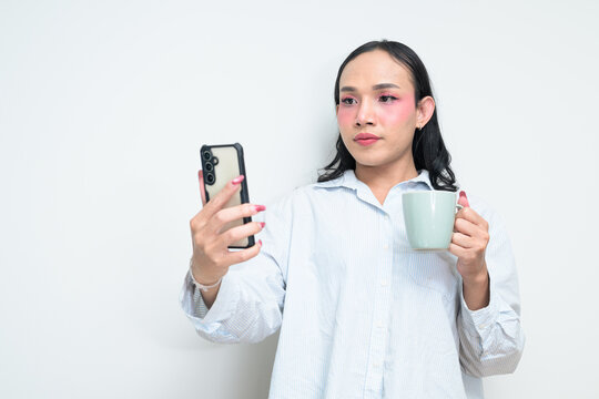 Portrait of Thai transgender person using phone and holding coffee cup against white background