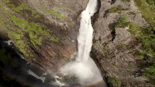 Aerial view of the powerful waterfall Manafossen cascading down between rocky cliffs, creating mist and a vibrant rainbow at its base, Dirdal, Rogaland, Norway.