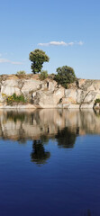Calm lakeside view on a clear day with gentle ripples reflecting surrounding rocks and grassy shore
