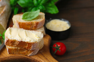 Slices of baguette with butter, basil and tomato on wooden table, closeup. Space for text