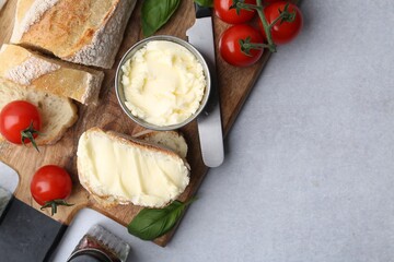 Cut baguette with butter, basil, tomatoes and knife on light table, flat lay. Space for text