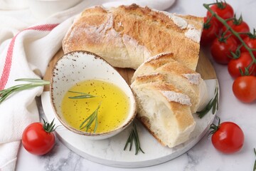 Tasty baguette served with oil, tomatoes and rosemary on white marble table, closeup