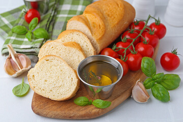 Tasty baguette served with oil, tomatoes and basil on white table, closeup