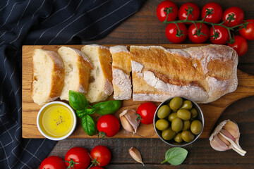 Tasty baguette served with oil, tomatoes, olives and basil on wooden table, flat lay