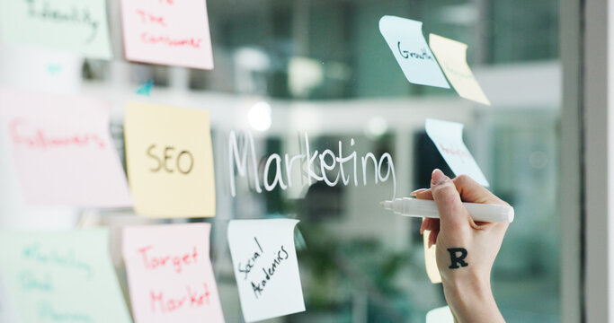 Advertising, hands and writing on glass wall for business growth, seo plan or target audience trends. Marketing, increase awareness and person at board with sticky note, strategy or goal for campaign