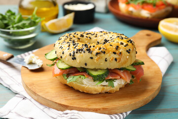 Delicious bagel with salmon, cream cheese, cucumber, arugula and lemon on light blue wooden table, closeup