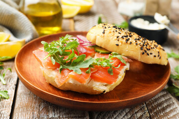 Delicious bagel with salmon, cream cheese, onion, arugula and lemon on wooden table, closeup