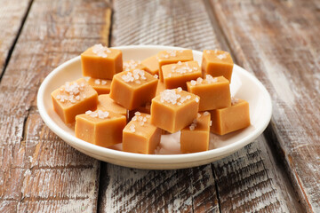 Tasty caramel candies with salt on color wooden table, closeup