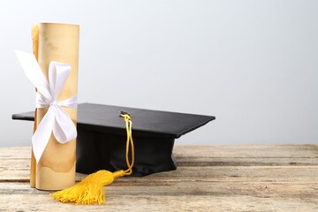 Graduation cap and diploma on wooden table against light background. Space for text