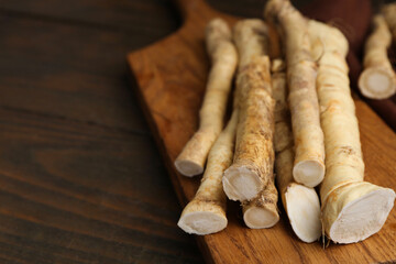Fresh raw horseradish roots on wooden table, closeup. Space for text