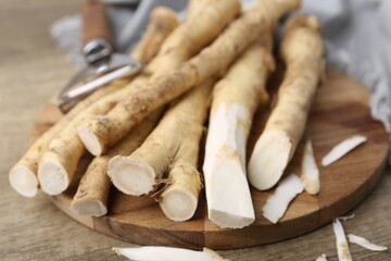 Fresh raw horseradish roots and peeler on wooden table, closeup