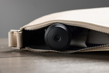 Hidden spy camera in purse on wooden table, closeup
