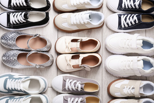 Many stylish kid's shoes on grey wooden floor, flat lay