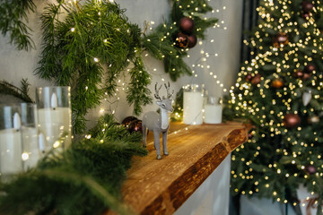 уютная комната с рождественской ёлкой, украшенной гирляндами и игрушками. На полке стоит фигурка оленя, зелёные ветки и свечи.
