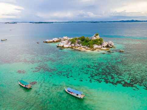 An aerial view of a tropical beach in Belitung, Indonesia. Small boats float on the sea, complementing the composition of clear turquoise blue water and small islands with rocks, white sand, and trees - Powered by Adobe