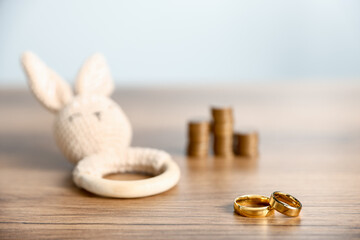 Alimony. Engagement rings, teething toy and coins on wooden table against light grey background, selective focus