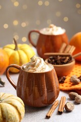 Tasty pumpkin latte with whipped cream in cups, spices and ingredients on light grey table against blurred lights, closeup. Bokeh effect